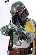 Homme dans une armure futuristique verte jaune et rouge usée, pointant un pistolet laser vers le photographe.
