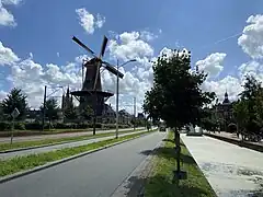 Photographie en couleurs d'une route traversant une ville, un moulin et des bâtiments constrits sur sa gauche.