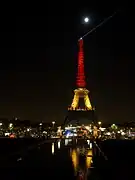 La Tour Eiffel illuminée de nuit, avec le haut de la tour rouge, le milieu jaune et le bas noir.