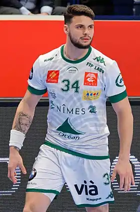 Photographie en couleur d'un homme en tenue de handballeur avec un ballon à la main.