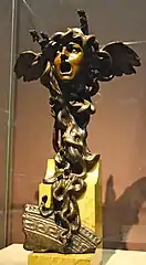 Sculpture. Masque de Méduse, la bouche grande ouverte, avec des ailes dans les cheveux ainsi que des lézards et des serpents entortillés qui lui servent de bas.