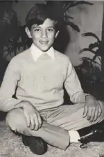 Photo noir et blanc d’un garçon d’une dizaine d’années assis par terre, avec un demi-sourire.