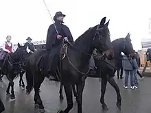 Cavaliers sur des chevaux noirs et portant des manteaux de pluie amples.