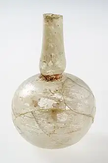 Photographie d'une petite fiole en verre, à la panse ronde et au bord allongé.