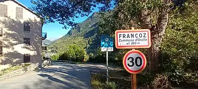 Photographie d'un panneau de Francoz, écrit en noir, où la limitation de vitesse est de 30 km/, devant des immeubles.