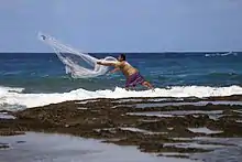 un homme lance un filet dans la mer, près du récif