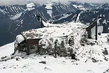 Petit bâtiment au design moderne sous la neige avec un paysage alpin en arrière-plan.