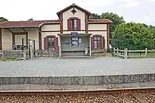 L'abri de quai de la halte avec les informations affichées. En arrière-plan, l'ancienne gare