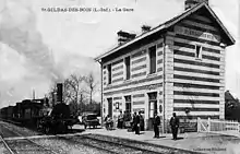 Le bâtiment voyageurs type à trois ouverture avec un train et une locomotive à vapeur qui arrive les cheminots et des voyageurs posent sur le quai