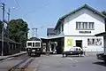 Be 4/4 26 marquant l'arrêt à quai et voiture de service 14 parquée devant l'ancienne gare d'Échallens en 1976.