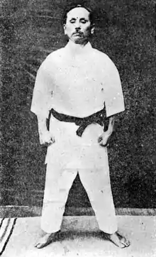 Gichin Funakoshi dans la position du yoi, qu'on retrouve au début de chaque kata Heian. Debout, pieds écartés de la largeur du bassin, bras le long du corps et poing serrés.