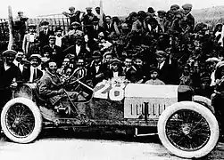 Photo de côté d'une voiture avec son pilote au volant avec des officiels de la course derrière