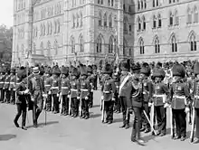 Photo en noir et blanc d'un dignitaire inspectant des militaires formés en uniforme