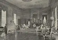 Photographie en noir et blanc d'un intérieur comportant des meubles et avec des boiseries sur les murs