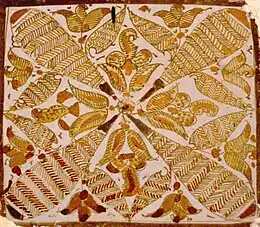 Photographie d'un carreau de céramique lustrée polychrome. Il présente une ornementation composée de feuillages et de hachures.