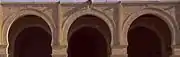 Photographie de trois arcs outrepassés de la façade du portique oriental de la cour. Ces derniers, appareillés en pierres de taille, sont encadrés de moulures et ornés d'un nœud à la clef.