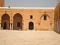 Vue de la partie du portique nord située à l'est du minaret, ouvrant sur la cour par deux arcades outrepassées brisées. À leur droite, la façade d'une salle à usage d'entrepôt.