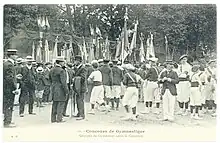 Photographie d'une foule parmi lesquels des groupes de gymnastes et des hommes portant des chapeaux, de nombreux drapeaux et bannières brandis en arrière-plan.