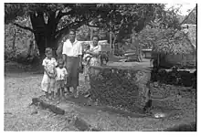 Photo en noir et blanc d'une famille composée d'un couple et trois enfants posant devant une large pierre rectangulaire