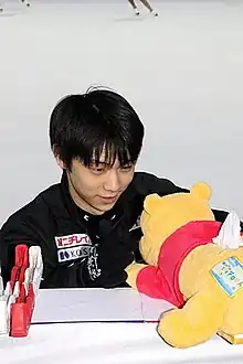 Un patineur asiatique et un ours jaune en peluche.