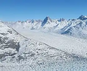 Photographie aérienne et en couleurs d'un glacier traversant une vallée encadrée de massifs montagneux.