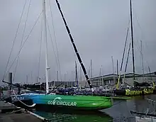 Vu de trois quarts avant, voilier à foils vert et bleu amarré au ponton.