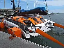 Voilier orangé et blanc vu de trois quarts arrière, amarré au ponton.