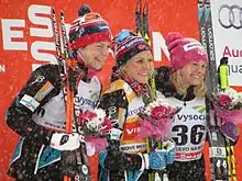 Trois skieuses, légèrement de profil, sur un podium, posant avec bouquets.