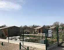 Photographie en couleurs d'un jardin, ceinturé d'un grillage, dans lequel se trouvent un cabanon et des tunnels de serres.