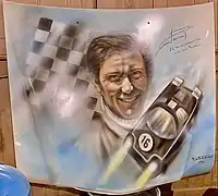 Jean-Pierre Jaussaud peint à l'Aérographe sur un capot de voiture exposé au Manoir de l'automobile. Le pilote a dédicacé l'œuvre où figure « sa » Rondeau M379B.