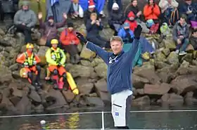 Debout à l'avant de son bateau, dans le chenal des Sables-d'Olonne, il salue la foule.