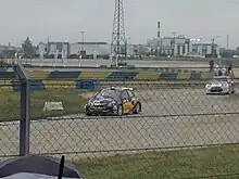 Sur une piste humide, une voiture noire roule.