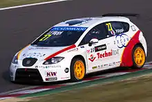 Voiture blanche vue de trois-quarts, sur des vibreurs rouges et blancs, à gauche de la piste.