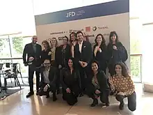 Photo en couleurs d'un groupe de 9 femmes et 3 hommes posant devant un panneau de logos d'entreprises.