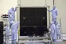 Un panneau solaire suspendu à un cadre et entouré de techniciens