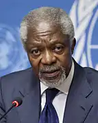 Photographie de Kofi Annan en 2012, représentant de l'Organisation des Nations unies, un homme de couleur de peau noire, aux cheveux et à la barbe blanche, portant un costume avec chemise blanche, veste et cravate bleues.