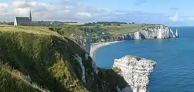 De grandes falaises blanches plongent dans la mer. Sur le plateau de terre, du bocage avec une église.