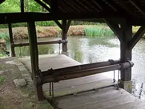 Photographie en couleurs d'un plancher et d'une toiture en bois surplombant un plan d'eau.