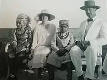 le roi et la reine en vêtements clairs posent assis sur un banc en compagnie de deux enfants