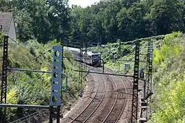 Vue d'un train et d'une ligne ferroviaire électrifiée à double voie construite en tranchée.