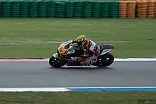 Vue de profil, d'une moto et son pilote fans un virage, la moto se dirigeant vers la gauche de la photo.