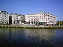 Vue de grands bâtiments blancs se reflétant dans un cours d’eau, sur fond de ciel bleu.