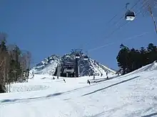 Photo couleur d'une station de télécabine au fond d'un plateau de montagne enneigé sous un ciel bleu.