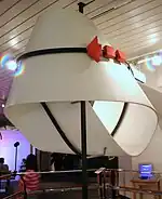 Photo d’une œuvre. Un ruban blanc torsadé agrémenté d’une flèche rouge.