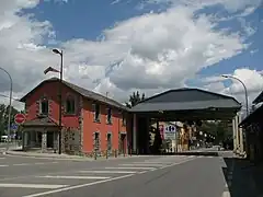 Vue d’un bâtiment aux murs rouges adossé à un préau surplombant une route.