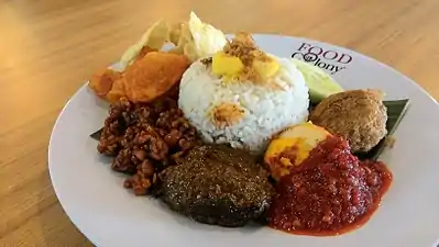 Bawang goreng sur un nasi lemak avec des emping, des perkedel kentang (boulettes de pomme de terre), de l'œuf avec une sauce pimentée, de la viande de bœuf, des kripik kentang, du tempe orek.
