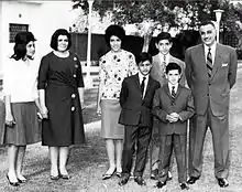Groupe familial prenant la pose dans un jardin. Nasser et ses fils portent des costumes et son épouse et ses filles portent des chemises et des jupes longues.
