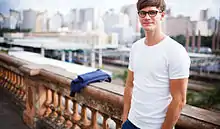 Un jeune homme souriant appuyé contre une balustrade.