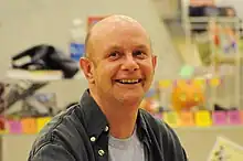 Portrait d'un homme chauve souriant prise dans une librairie.