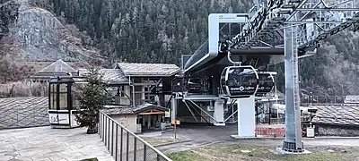 Photographie de cabines dans une gare et d'une vieille cabine qui est présente sur un balcon de bâtiment, le tout au pied de la montagne.